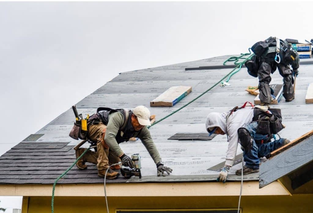 Roofers repairing a residential roof by installing shingles and underlayment.